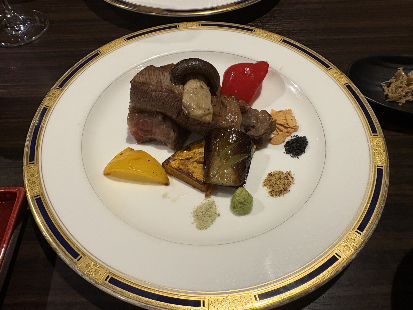 2026-09-21 演出鉄板 ココットアルファ「煌めき」コースの鉄板焼き。金彩の皿に牛肉・椎茸・かぼちゃ・パプリカと、4種の塩と薬味が添えられている